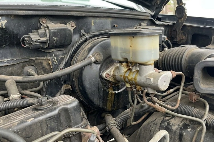 Brake master cylinder mounted on a vehicle firewall showing fluid reservoir and hydraulic brake lines