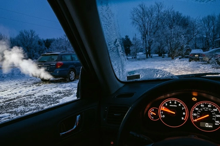 Car parked outside on a cold winter morning with frost on the windshield, engine running rough at idle with exhaust vapor visible, the dashboard tachometer needle visibly bouncing.