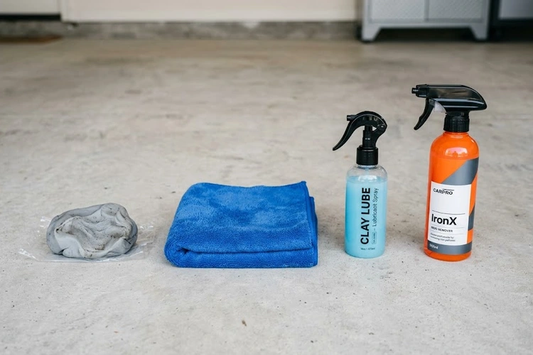 Clay bar and iron remover spray bottle placed side by side on a car hood for comparison