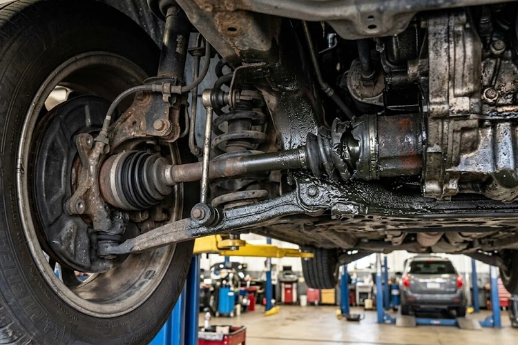 CV axle noise symptoms — mechanic inspecting front axle CV boot for cracks and grease leaks