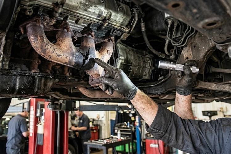 Mechanic inspecting exhaust manifold closely for exhaust leak symptoms and soot deposits