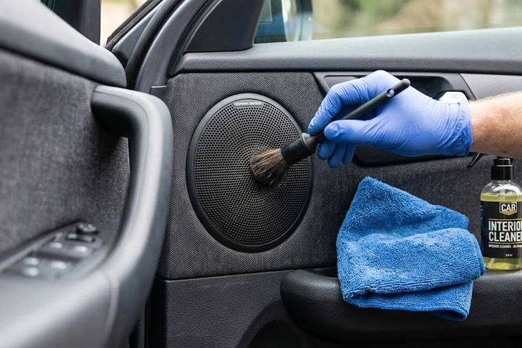 Detailing brush gently cleaning a car door speaker grille to remove dust without damaging the cone