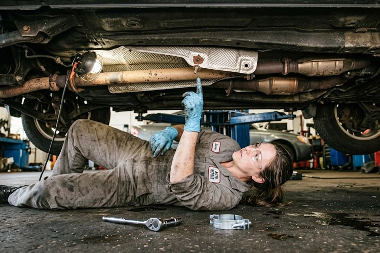 Mechanic inspecting a corroded heat shield mounting tab during a rattling heat shield fix