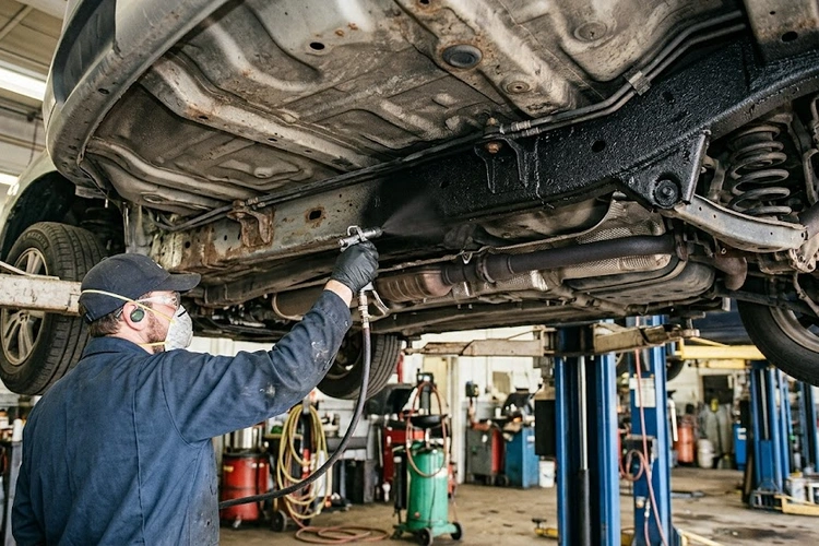technician applying rubberized undercoating to car underbody to protect metal from rust