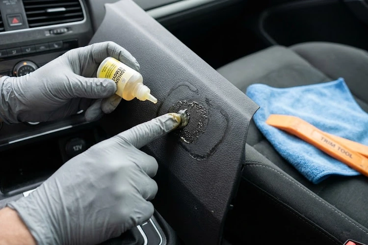 Sticker residue on a car interior dashboard panel being treated with isopropyl alcohol and a microfiber cloth